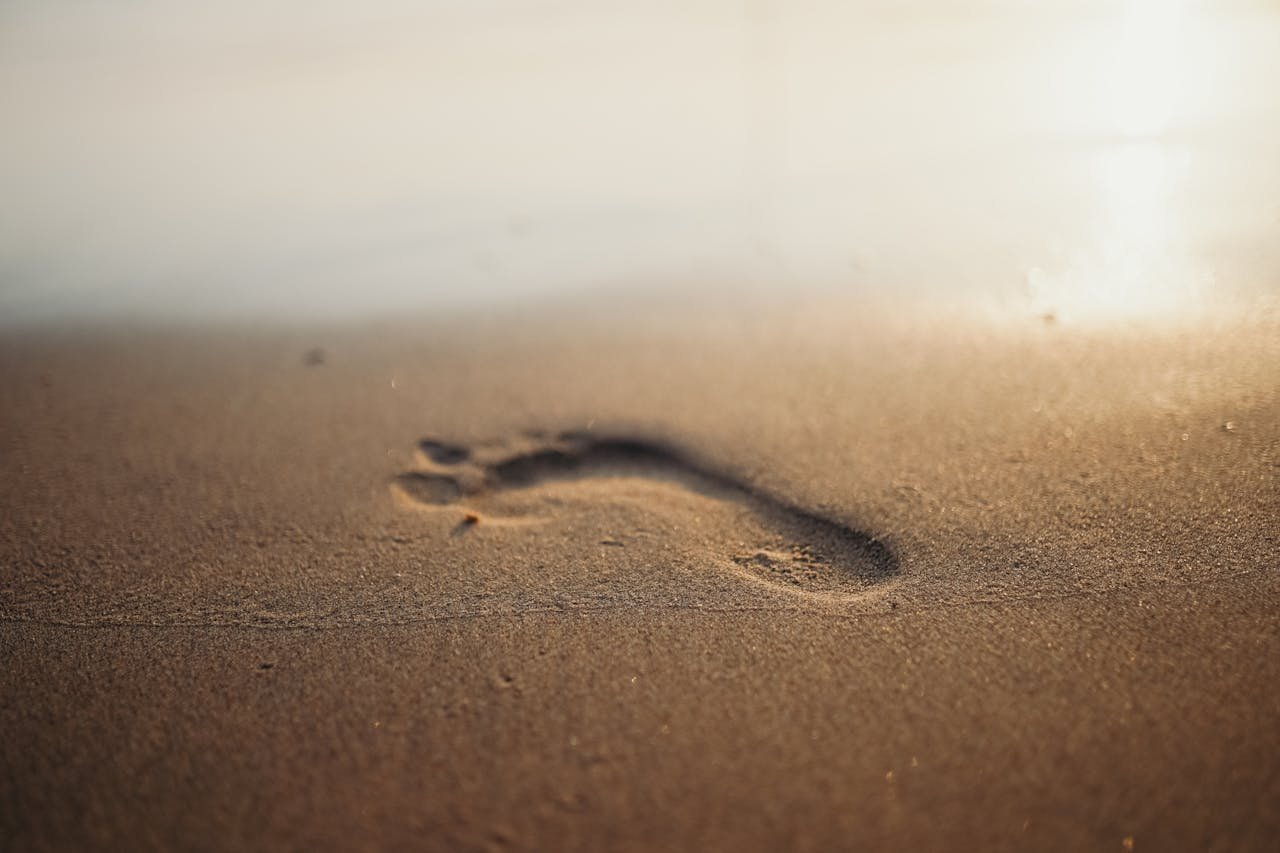Footprint on sandy beach during sunrise, evoking calm and relaxation.